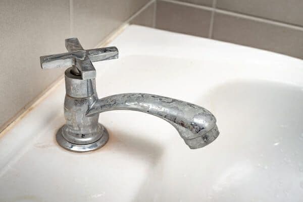 A bathroom sink faucet with visible lime and mineral deposits on the metal surface