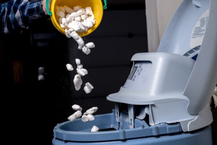 Pouring fresh salt into the water softener system during routine maintenance