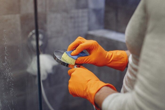 Person cleaning showerhead free of scale buildup with salt-free softening system