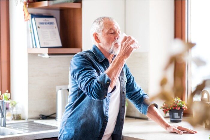 Older man drinking a glass of soft water in a kitchen setting
