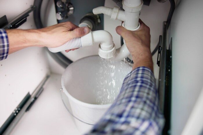 Plumber fixing a leaking pipe under the sink to reduce water waste