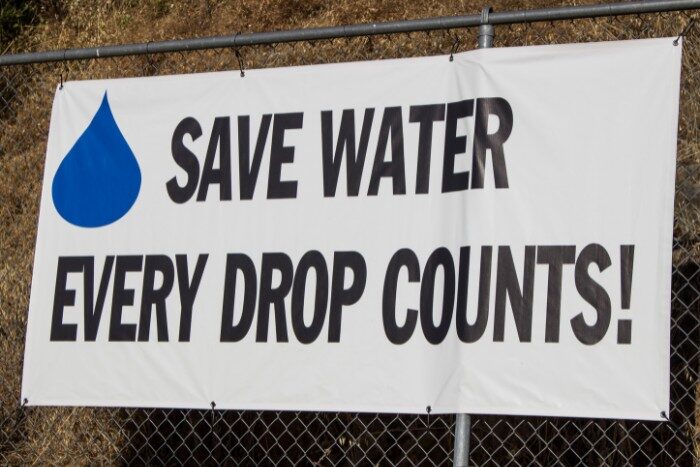 Banner reading “Save Water Every Drop Counts” displayed on fence