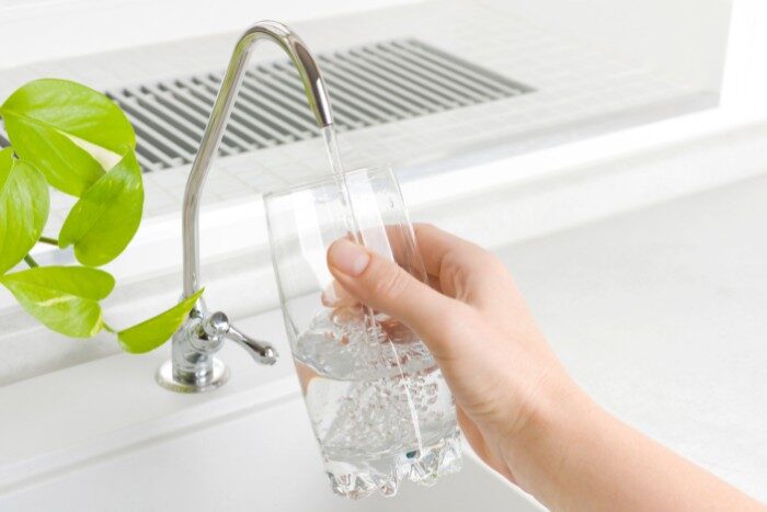 Hand filling a glass with filtered drinking water from a kitchen tap