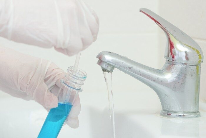 Gloved hands collecting water sample for professional water hardness testing