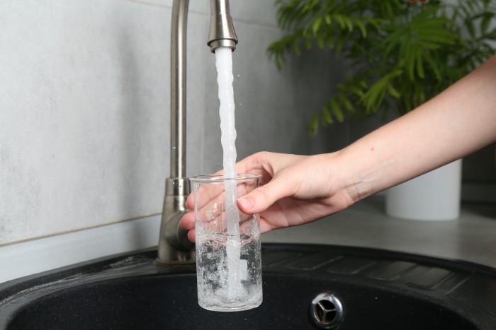 Collecting tap water in a glass for a home water hardness test