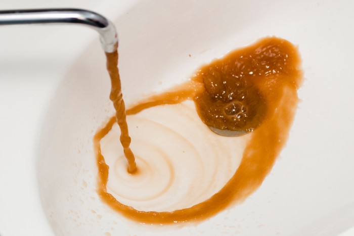 Rust colored water flowing into a white sink due to corroded anode rod